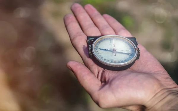 Elinde pusula tutan bir erkek var. Avucunun içinde eski bir pusula tutan adam yön gösteriyor. Açık hava fotoğrafı, yakın plan, bulanık arkaplan.