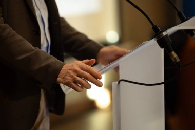 Politik bir miting, sempozyum veya toplantı sırasında kürsüden konuşma yapan bir mikrofona ve bir hoparlörün ellerine odaklanın.