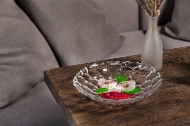 Pancar suyunda turp dilimleri ve karabuğday taneleriyle kaplı levrek tartar. Yemek şeffaf bir tabakta, siyah, ahşap bir masada yatıyor..