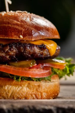 Biftek köfteli çizburger, marul ve hardal soslu taze domates. Yakınlarda kızarmış patates ve domates turşusu var. Yiyecek, arka planda, ahşap bir tezgahta yatıyor..