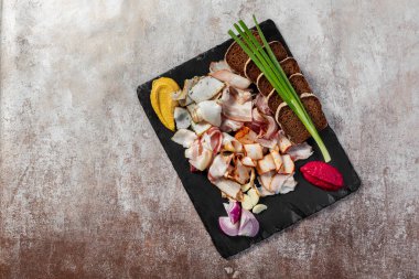 Domuz pastırması, tütsülenmiş et ve fırında et. Yeşil soğan, hardallı siyah ekmek tostu ve siyah bir tabakta pancar pancarı. Plaka hafif bir arkaplanda duruyor..