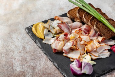 Domuz pastırması, tütsülenmiş et ve fırında et. Yeşil soğan, hardallı siyah ekmek tostu ve siyah bir tabakta pancar pancarı. Plaka hafif bir arkaplanda duruyor..