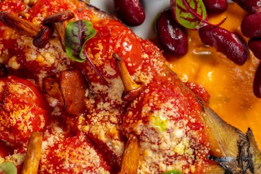 Baharatlı biber soslu domates ve peynirli patlıcan, mantarlı ve fındıklı. Balkabağı püresi ve kırmızı fasulyelerin yanında. Hafif seramik tabakta yemek. Plaka hafif bir arkaplanda duruyor..