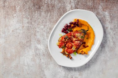 Baharatlı biber soslu domates ve peynirli patlıcan, mantarlı ve fındıklı. Balkabağı püresi ve kırmızı fasulyelerin yanında. Hafif seramik tabakta yemek. Plaka hafif bir arkaplanda duruyor..