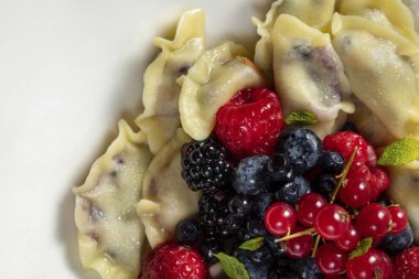 Böğürtlen, yabanmersini, ahududu ve hafif arkaplanda hafif seramik bir tabakta kırmızı frenk üzümü ile süslenmiş kiraz köfteleri..