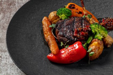 Sebze havuçlu ızgara fileminyon biftek, kiraz soslu paprika brokoli. Yiyecek, arka planda karanlık bir levhada yatar..