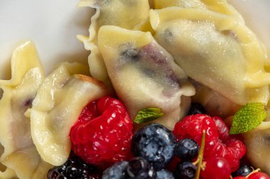 Böğürtlen, yabanmersini, ahududu ve hafif arkaplanda hafif seramik bir tabakta kırmızı frenk üzümü ile süslenmiş kiraz köfteleri..