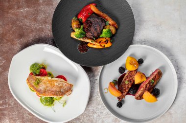 Üç yemek hazır. Sebzeli fileminyon, domatesli levrek ve pesto ve böğürtlenli ördek göğsü açık arkaplanda seramik tabaklarda yatıyor..