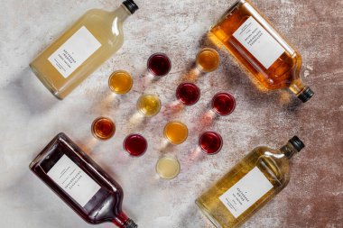 Çeşitli ev yapımı bal likörü, yabanturpu ve galangal. Tentürler bardaklara dökülüyor, yakınlarda birkaç şişe var. Herkes hafif bir arka planda durur..