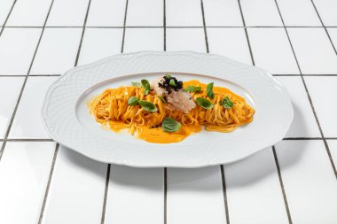 Peynir soslu spagetti ve ince doğranmış soğanlı tartar ve hafif seramik tabakta siyah havyar. Plaka hafif bir arkaplanda duruyor..