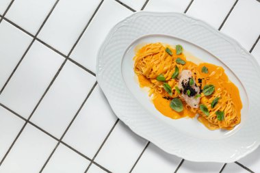 Peynir soslu spagetti ve ince doğranmış soğanlı tartar ve hafif seramik tabakta siyah havyar. Plaka hafif bir arkaplanda duruyor..