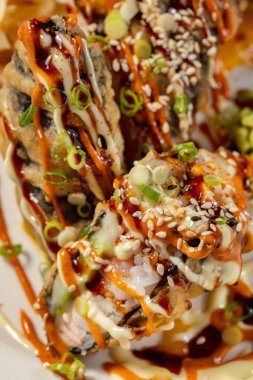 Pirinçli sıcak rulo, unagi soslu füme yılan balığı Japon mayonezli ve kırmızı biberli. Yakınlarda bir parça wasabi ve bir miktar zencefil var. Yiyecek hafif bir zemin üzerinde seramik bir tabakta yatıyor..