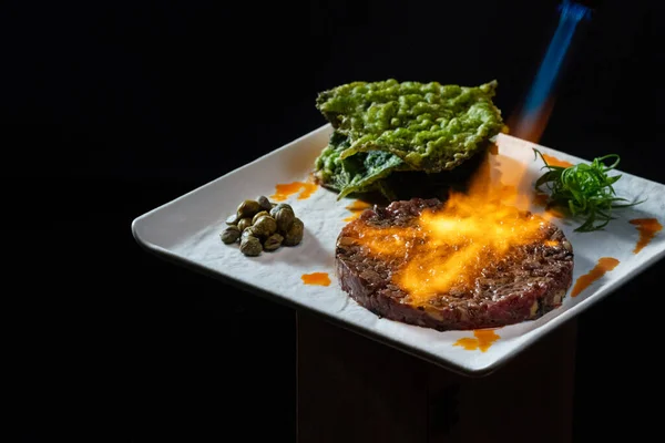 瓦格纳牛肉薄荷叶与可食用的天麻叶 胡瓜和海藻附近 食物放在深色背景的正方形瓷盘上 — 图库照片