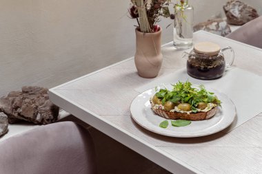 Karabuğday ekmeğinde ringa balığı turşulu üzüm, nane yaprağı ve kişniş. Yiyecek seramik tabakta yatıyor. Plaka hafif bir arkaplanda duruyor..