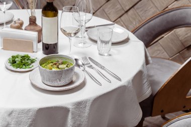 Dana eti, patates, ıspanak ve bıldırcın yumurtalı yeşil borş çorbası. Çorba hafif bir seramik tabağa dökülüyor, yanında yeşil bir kapak, bir şişe ve bir bardak beyaz şarap var..