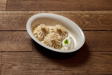 Khinkali ve kuzu kıyması. Sos ve Gürcü baharatları. Yemekler oval, hafif seramik tabakta, yanında da soğan yağlı kremalı sos var..