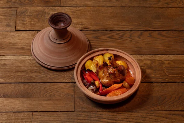 Leg of lamb baked with potatoes, paprika, carrots and red onions in a ceramic dish with a lid.