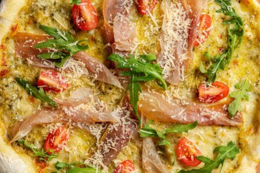 Prosciutto, roka, vişneli domates ve rendelenmiş parmesanlı ekşi pizza. Pizza gri bir arka planda yatıyor..