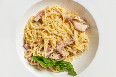 Ev yapımı Carbonara makarnası et, peynir, kremalı sarımsak sosu gri taştan bir arka planda açık seramik tabakta.
