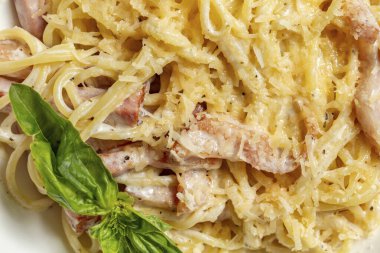 Ev yapımı Carbonara makarnası et, peynir, kremalı sarımsak sosu gri taştan bir arka planda açık seramik tabakta.