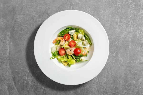 stock image Summer mix salad with dor blue cheese, shrimp, cherry tomatoes and olive oil. The salad lies in a light ceramic plate on a gray stone background.