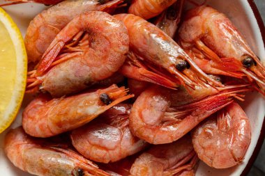 Birayla kızartılmış karidesler ve gri taşlı arka planda seramik tabakta bir dilim limon..