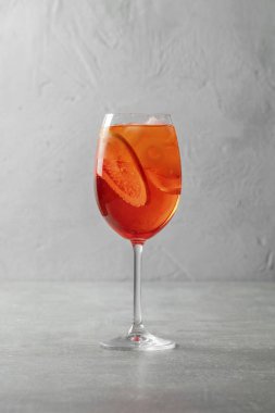 Portakal dilimli Aperol Spritz kokteyli ve gri taştan bir arka planda şeffaf uzun cam bir kadehte buz parçaları..