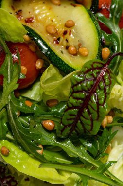 Sebze salatası, kabak, kiraz domatesleri, çam fıstığı, zeytinyağı ve balzamik sos. Yiyecek, renkli bir zemindeki açık seramik bir tabakta yatıyor..