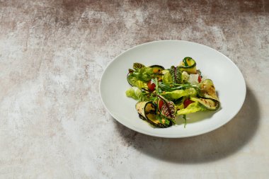 Sebze salatası, kabak, kiraz domatesleri, çam fıstığı, zeytinyağı ve balzamik sos. Yiyecek, renkli bir zemindeki açık seramik bir tabakta yatıyor..