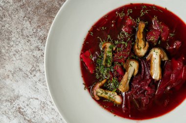 Ukrayna çorbası çorbası, hafif seramik tabakta mantar ve sebzelerle birlikte. Yakınlarda kızarmış patates ve yeşil soğanlı bir levha var. Tabaklar hafif kumaş arkaplanda durur.