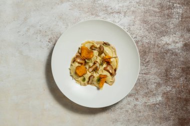 Patatesli börek, kızarmış mantar ve patates cipsi en üstte. Yiyecek kumaş zemin üzerinde hafif bir seramik tabakta yatıyor..