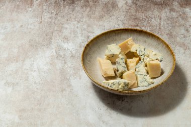 Ukrayna parmesan peyniri ve dorblyu peyniri parçalanmış ve seramik bir tabakta açık kumaş arka planda yatıyor..