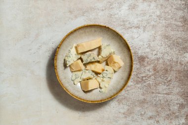 Ukrayna parmesan peyniri ve dorblyu peyniri parçalanmış ve seramik bir tabakta açık kumaş arka planda yatıyor..