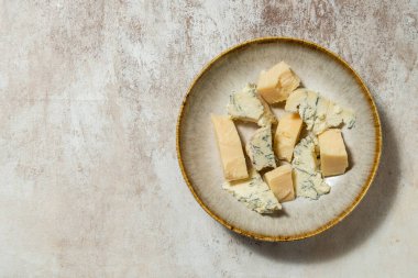 Ukrayna parmesan peyniri ve dorblyu peyniri parçalanmış ve seramik bir tabakta açık kumaş arka planda yatıyor..