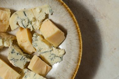 Ukrayna parmesan peyniri ve dorblyu peyniri parçalanmış ve seramik bir tabakta açık kumaş arka planda yatıyor..