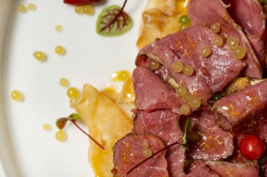 Pastırmalı ev yapımı krep, marul yaprağı ve hafif seramik trilke üzerine çilek sosu. Plaka hafif bir kumaş zemin üzerinde duruyor..