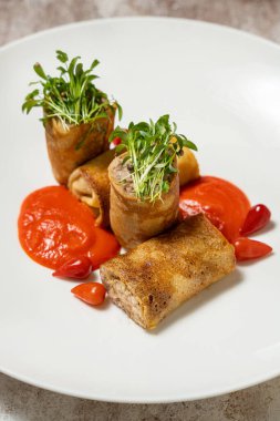 Tavşan etli gözleme, mikroyeşil lahanalar, domates sosu ve kırmızı biber. Yiyecek hafif bir seramik tabakta, hafif bir kumaş arkaplanda yatıyor..