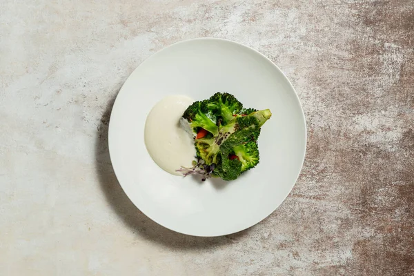 stock image Half of grilled broccoli with chili pepper and radish puree. Food lies in a light ceramic plate on a light fabric background.