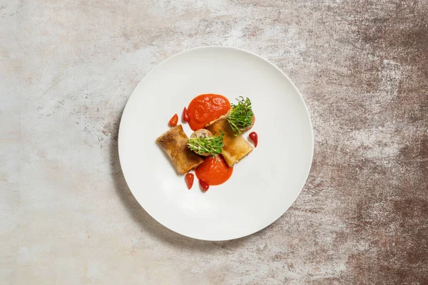 Pancakes with rabbit meat, microgreen sprouts, tomato sauce and chili pepper. Food lies in a light ceramic plate on a light fabric background.