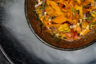 Koyu seramik tabakta kabak cipsli deniz ürünleri salatası. Tabak, taşlarla ve kuru buzdan gelen dumanla karanlık bir formda. Tabaklar siyah kadife koltukta oturur..