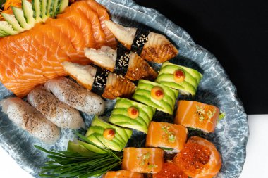 Avokado, yılan balığı, somon, kırmızı havyar, oval seramik tabakta bulunan mavi desenli mavi ve beyaz kağıtlı çeşitli suşi çeşitleri. Yanında alçı bir heykel var..