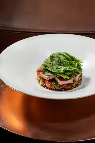 在莴苣叶下切碎的金枪鱼牛排 放在奎诺阿和蔬菜的塔布上 食物放在靠近椅子的青铜桌子上的一个轻质陶瓷盘里 — 图库照片