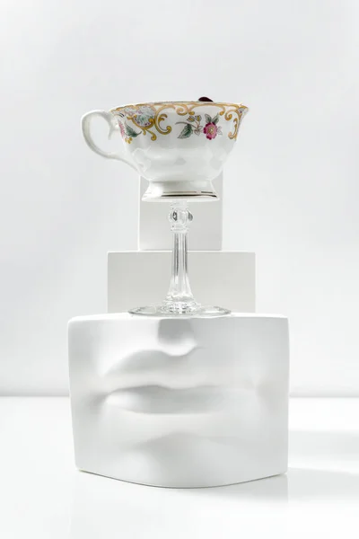 Rock Island cocktail with raspberry powder and grapes on a skewer. A cocktail in a glass in the shape of a cup on a long stem stands on a plaster figure among plaster figures on a white background.