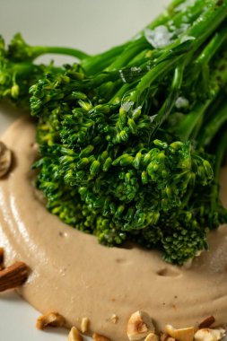 Ceviz soslu ızgara brokoli ve hafif seramik tabakta fıstık. Tabak bir bardak beyaz şarap ve çatal bıçak sehpasının yanında hafif bir masa örtüsünün üzerinde duruyor..