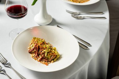 Kurutulmuş domatesli ıspanaklı makarna ve hafif seramik tabakta doğranmış yeşil soğanlı fındık. Tabak bir bardak kırmızı şarap ve çatal bıçak takımının yanında hafif bir masa örtüsünün üzerinde duruyor..