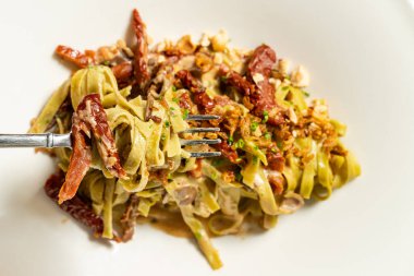 Kurutulmuş domatesli ıspanaklı makarna ve hafif seramik tabakta doğranmış yeşil soğanlı fındık. Tabak bir bardak kırmızı şarap ve çatal bıçak takımının yanında hafif bir masa örtüsünün üzerinde duruyor..