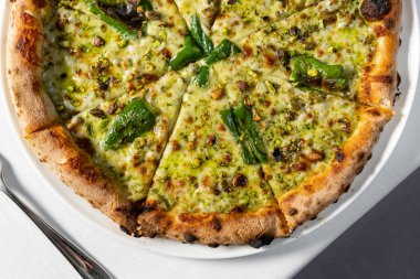 Ekşi hamurlu pizza, dört peynirli jalapeno ve şam fıstığı ve hafif seramik tabakta parmesan peyniri. Tabak bir bardak beyaz şarabın yanında hafif bir masa örtüsünün üzerinde duruyor..