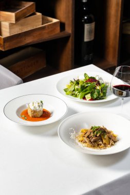 Güneşte kurutulmuş domatesli ıspanaklı makarna stracciatella peynirli patlıcan ve pancar salatası ve hafif bir masa örtüsünün üzerinde Gorgonzola. Yakınlarda bir kadeh kırmızı şarap var..