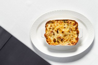 Sebze, üzerinde rendelenmiş parmesan peyniri olan seramik bir tabakta ev yapımı lazanya. Tabak açık masa örtüsü olan bir masanın üzerinde..