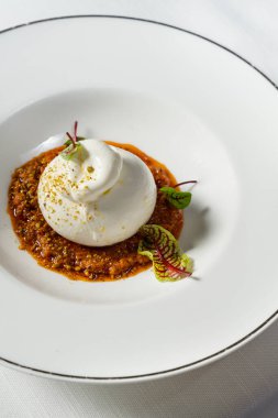 Marullu bufalo mozzarella. Sebze yahnisi, fındık ve şarap sosu. Yemek seramik tabakta yatıyor. Tabak bir bardak beyaz şarap ve çatal bıçak takımının yanında hafif bir masa örtüsünün üzerinde duruyor..